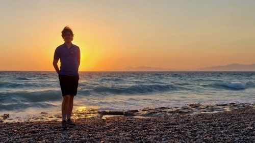 A photo of me on a windswept beach against a sunset.